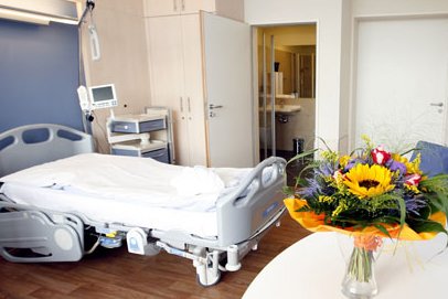 Patientenzimmer mit Pflegebett, Tisch und Besucherstühlen